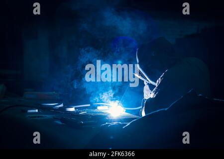 Schweißer in Helm und Maske bei der Arbeit in der industriellen Metallurgie Fabrik, close up in blauer Farbe. Stockfoto