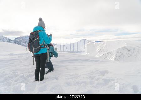 Kasprowy Wierch, Polen 28.01.2021 - zwei Bergsteiger auf dem Gipfel, die schöne Szenen vor ihnen fotografieren. Schneebedeckte Berge vor dem weißen Himmel in der Winterlandschaft. Stockfoto