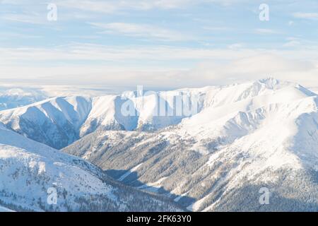 Wunderschöne Panoramaaufnahme der schneebedeckten Wintergipfel während der Wintersaison gegen den wolkig-blauen Himmel. Verschneite Berge in der Stadt Zakopane - Kasprowy Wierch. Hohe Qualität Stockfoto