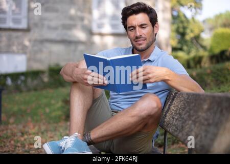 Der junge Mann, der ein Buch las, saß draußen auf einer Bank Stockfoto