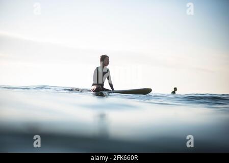 Asiatische Frau wartet auf Wellen während Sonnenaufgang Sommer Surf Session Stockfoto