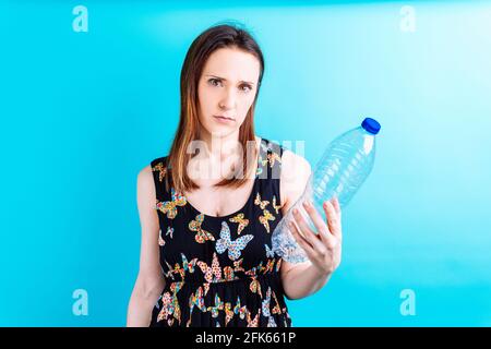 Schöne junge Frau mit wütend Ökologen Gesicht hält eine Plastikflasche Wasser. Konzept vermeiden Kunststoff. Kontamination. Recycling und Ökologie Stockfoto