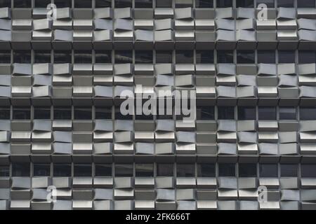 Eine graue Fassade eines modernen Bürohochhauses Mit Reihen von Fenstern und vielen kleinen Betonblöcken Jeder hat seinen eigenen zufallshori Stockfoto