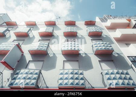 Blick von unten auf eine bläuliche Wohnhausfassade mit einer regelmäßigen Struktur aus kleinen rechteckigen Balkonen mit einem gefliesten Muster auf ihren Zäunen; A Stockfoto