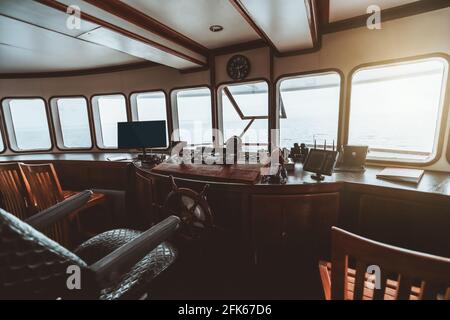 Weitwinkelansicht einer Kapitänskabine auf der Yacht mit einem Armaturenbrett im Holzkeller mit Monitoren, Navigationsausrüstung und Lenkrad auf i Stockfoto