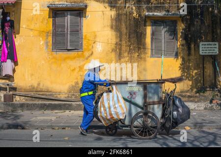 Vietnamesischer Müllsammler schiebt Müllwagen entlang der Straße in der Altstadt von Hoi an, Vietnam Stockfoto