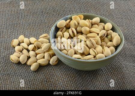 Pistazien in Schalen in Keramik-Snack-Schale auf grau Sackleinen Stockfoto