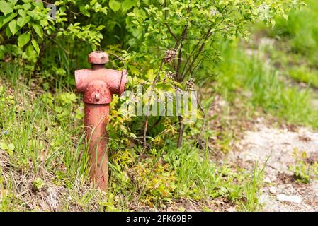 Alter roter Hydrant. Ein angeschlagener Hydrant steht an der Seite einer Dorfstraße. Frühling in Polen bei Krakau. Stockfoto
