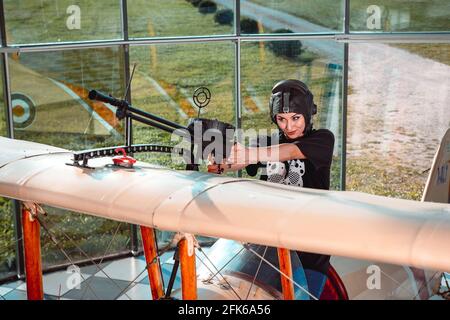 Frau mit einem Pilotenhelm, die mit einem Maschinengewehr spielt Montiert auf einer Nachbildung eines Weltkriegsflugzeugs Stockfoto