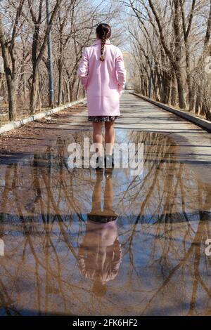 Im Frühling steht ein Mädchen in einer Pfütze mit einem Spiegelbild von Bäumen Stockfoto