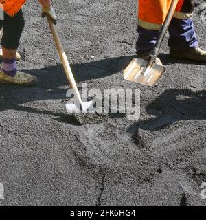 Straßenreparaturarbeiten. Arbeiter gleichen den Asphalt mit Schaufeln. Bauarbeiter während der Asphaltstraße. Handarbeit im Bauwesen Stockfoto