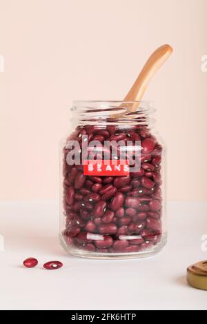 Rote Bohnen im Glas mit Holzlöffel auf beige und weißem Hintergrund. Health care Lifestyle und Bio-Food-Konzept. Stockfoto