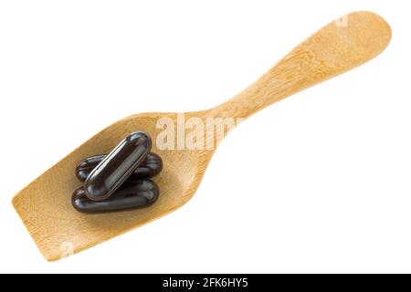 Draufsicht auf 3 dunkelschwarze Arznei-Weichgel-Kapseln Auf Holzlöffel isoliert auf weißem Hintergrund Stockfoto