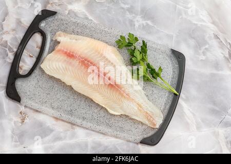 Filet aus rohem Pangasius-Fisch mit Petersilienblättern auf Schneidebrett. Draufsicht. Stockfoto