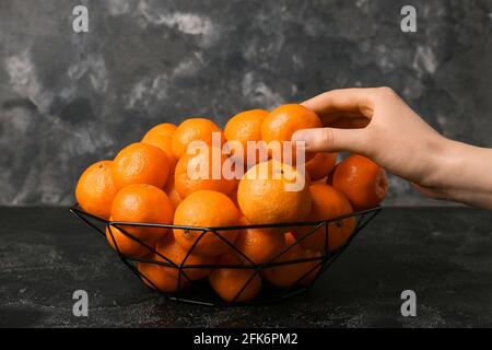 Frau nimmt süße Mandarine aus dem Korb auf dunklem Hintergrund Stockfoto
