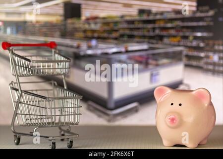 Pink Piggy Bank Schwein steht in der Nähe Mini-Shopping Push-Cart Mit verschwommenem Supermarkthintergrund Stockfoto