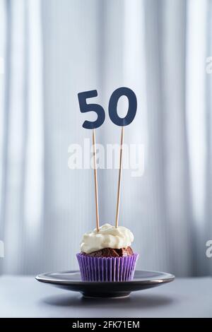 Digitales Geschenkkarten-Jubiläumskonzept. Leckere hausgemachte Schokolade Geburtstag Cupcake mit weißen cremigen Belag und Nummer 50 fünfzig mit hellen Hintergrund in minimalistischem Stil. Hochwertiges vertikales Bild Stockfoto