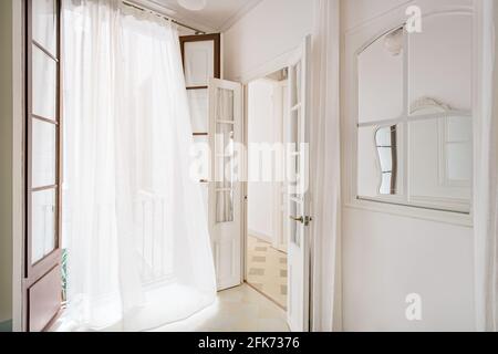 Weißer winkender Vorhang in leerem Zimmer der renovierten Wohnung in Barcelona. Einrichtung im klassischen Stil mit Fenster und Spiegel. Stockfoto