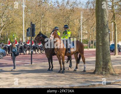 Zwei weibliche Polizisten der Metropolitan-Polizei beritteten in der Mall, London, England, Großbritannien, Offiziere zu Pferd. Berittene Soldaten der Hauskavallerie kommen vorbei. Stockfoto