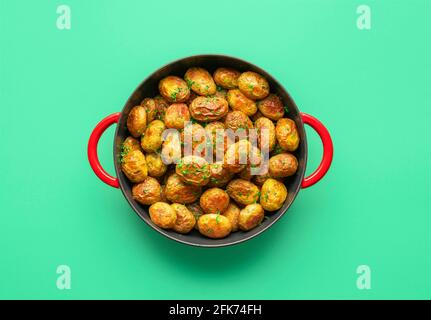 Gebratene Babykartoffeln in einer gusseisernen Pfanne minimalistisch auf einem grünen Tisch. Draufsicht mit einem Kartoffelgericht in einer Pfanne auf einem farbigen Hintergrund isoliert gebacken Stockfoto