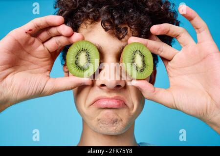 Mann mit lockigem Haar, der Kiwi in der Nähe des Klassengesichts hält Emotionen Stockfoto