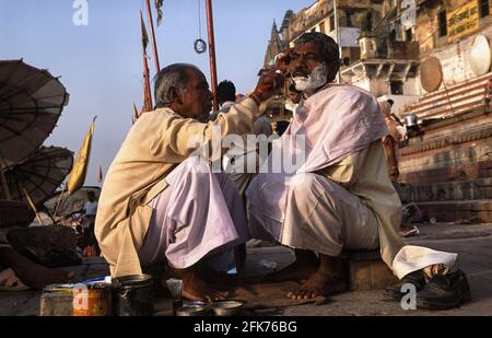 24.03.2010, Varanasi, Uttar Pradesh, Indien, Asien - EIN Straßenbarbier rasiert einen Kunden in den frühen Morgenstunden an einem Ghat entlang des heiligen Ganges. Stockfoto