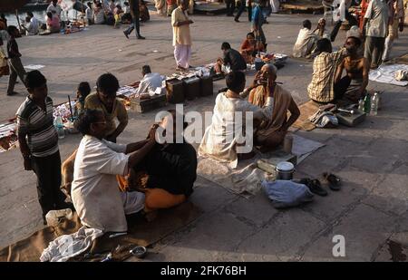 24.03.2010, Varanasi, Uttar Pradesh, Indien, Asien - Straßenbarbiere rasieren Kunden in den frühen Morgenstunden an einem Ghat entlang des heiligen Ganges Flusses. Stockfoto