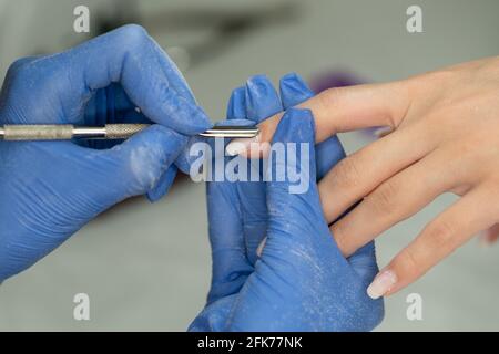 Manikurist macht Maniküre in blauen Handschuhen für Kunden im Schönheitssalon. Schuppenschicht mit Spachtel. Medizin, Kosmetologie und Maniküre. Stockfoto