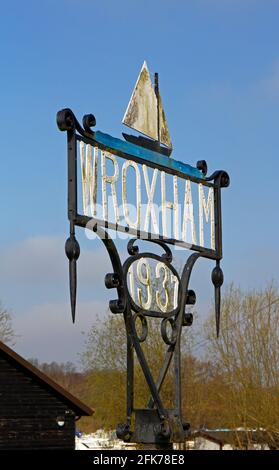 Ein Wroxham Village Schild an der A1151 Straße bei der Brücke über den Fluss Bure in Wroxham, Norfolk, England, Vereinigtes Königreich. Stockfoto