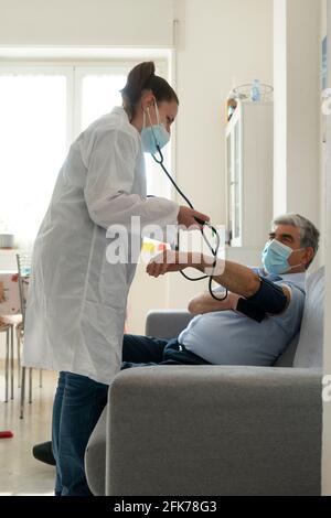 Eine junge Ärztin überprüft den Blutdruck bei einem alten Mann Zu Hause Stockfoto
