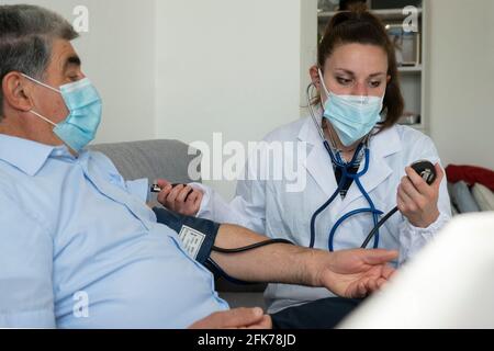 Eine junge Ärztin überprüft den Blutdruck bei einem alten Mann Zu Hause Stockfoto