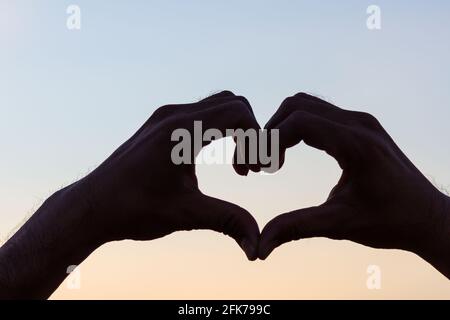 Liebeszeichen. Herz-Symbol von Hand Silhouette in Sonnenuntergang Himmel. Hintergrund im Vintage-Stil Stockfoto