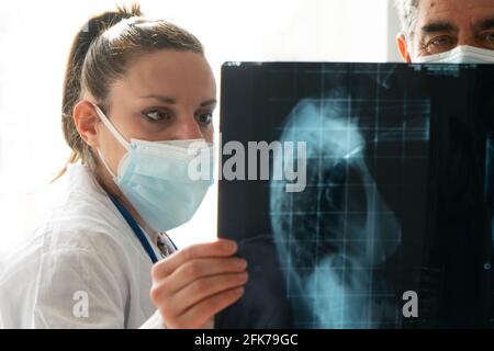 Junge Ärztin mit leitendem Arzt prüft eine Röntgenaufnahme. Konzept der Zusammenarbeit zwischen jungen Ärzten und erfahrenen Ärzten. Stockfoto