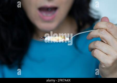 Eine Frau mittleren Alters nimmt einen Löffel voller Pillen. Konzept der Drogenabhängigkeit oder Notwendigkeit, viele Drogen zu nehmen. Stockfoto