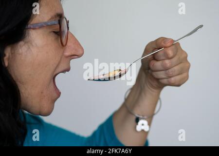 Eine Frau mittleren Alters nimmt einen Löffel voller Pillen. Konzept der Drogenabhängigkeit oder Notwendigkeit, viele Drogen zu nehmen. Stockfoto