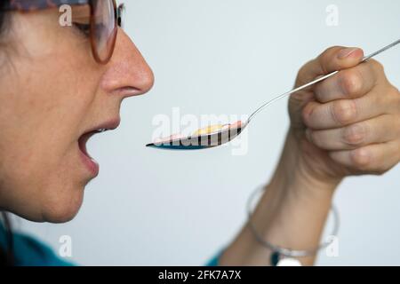 Eine Frau mittleren Alters nimmt einen Löffel voller Pillen. Konzept der Drogenabhängigkeit oder Notwendigkeit, viele Drogen zu nehmen. Stockfoto