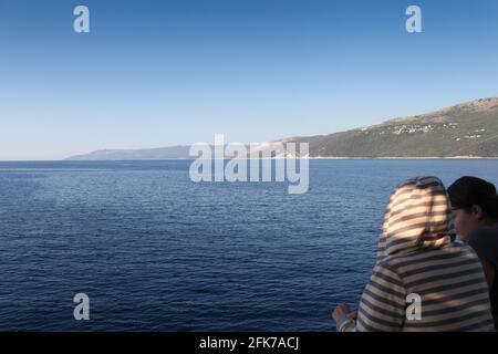 Zwei Leute beobachten das Meer von einer Fähre aus an einem Sommermorgen. Der Himmel ist blau, das Meer ist ruhig. Stockfoto