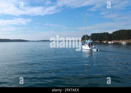 Ein Segelboot geht auf einem ruhigen blauen Meer hinaus, Inseln umgeben das Boot. Stockfoto