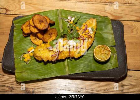 Ein köstliches Gericht aus westafrikanisch inspiriertem gebratenen Fisch und Pommes mit gebratenen Bananenscheiben auf einem Bananenblatt serviert Stockfoto