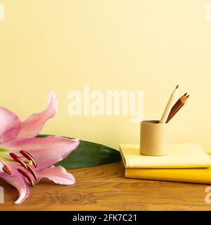 Notizbuch, Buntstifte, Blume auf Holzschreibtisch. Gelber Hintergrund. Arbeits- und Studienort Stockfoto