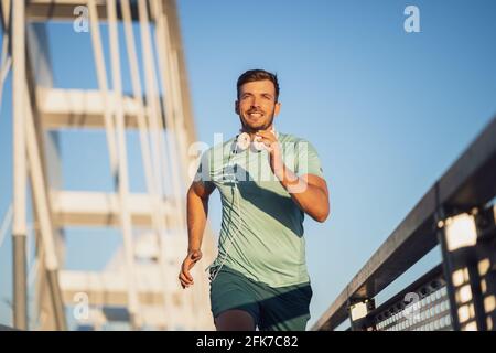 Junger glücklicher Mann joggt draußen auf der Brücke in der Stadt. Stockfoto