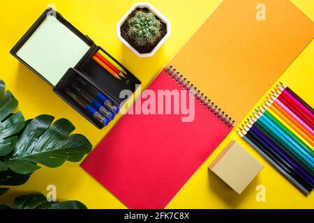 Layout von mehrfarbigen Papeterie auf gelbem Hintergrund: Spiralheft, Buntstifte, Ständer, Stifte, Innenblume. Business Flat Lay, Mock Up. S Stockfoto