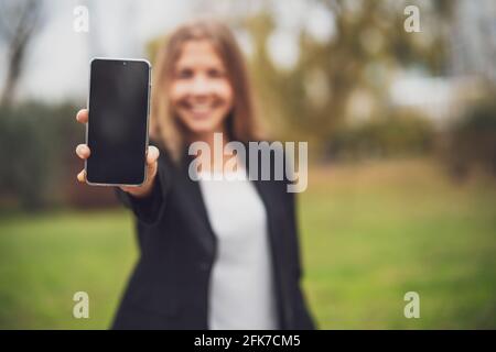 Außenportrait der glücklichen Geschäftsfrau, die Smartphone mit leerem Bildschirm hält. Stockfoto