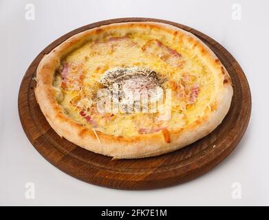 Blick von oben auf heiße Pizza auf einem Holzständer. Pizza Carbonara mäßig getoasteter Speck, bedeckt mit Parmesankäse, zwei Käsesorten und an der Spitze complemen Stockfoto