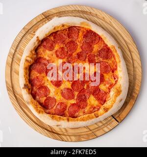 Blick von oben auf heiße Pizza auf einem Holzständer. Pepperoni Pizza. Tomatenbasis, zwei Käsesorten und viel Salami. Stockfoto