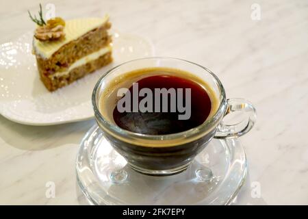 Nahaufnahme einer Tasse heißen Kaffee mit verschwommener hausgemachter Karotte Kuchen im Hintergrund Stockfoto