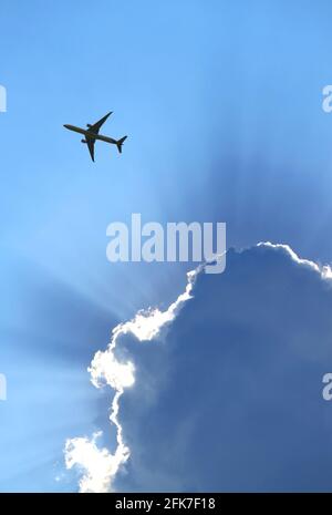 Silhouette des Flugzeugs fliegen in den blau bewölkten Himmel mit Tolle Sonnenstrahlen Stockfoto