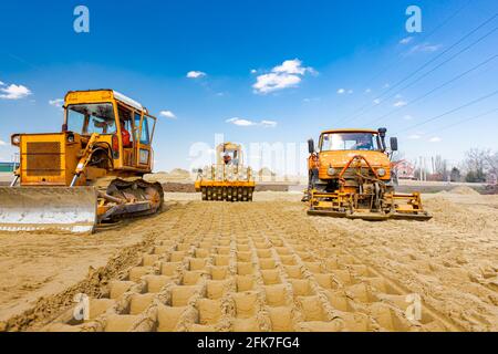 Straßenwalze mit Spikes, Planierraupe und LKW mit montiertem Plattenschwingungsverdichter verdichten und nivellieren Sand für Straßenfundamente auf der Baustelle Stockfoto