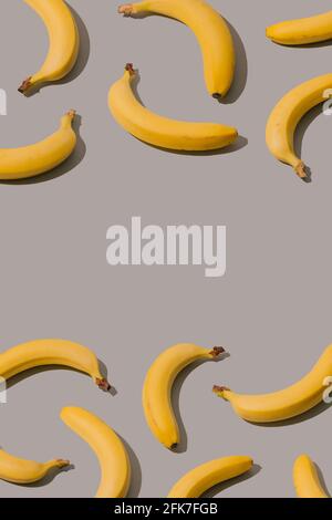 Kreatives Muster mit gelben Bananen auf grauem Hintergrund. Minimale abstrakte ästhetische Idee. Stockfoto