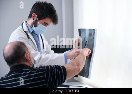 Junger Arzt, der die Röntgenaufnahme eines älteren Patienten untersucht. Radiographie einer Wirbelsäule, Wirbelsäule oder Wirbelsäule. Stockfoto